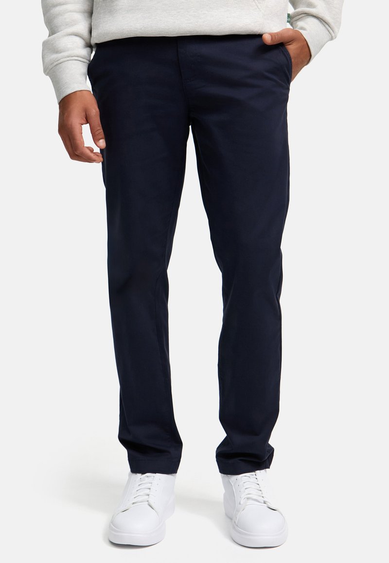 Chinos azul marino de tela ligera, con un diseño de pierna recta, frente plano, bolsillos laterales y combinados con zapatillas blancas.