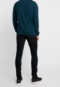 Teal neule pitkähihaisilla hihoilla, ribattuja hihansuut ja helma, yhdistettyinä slim-fit mustiin farkkuihin ja mustiin lenkkareihin, joissa on valkoiset pohjat.