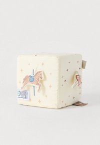 Μαλακό παιχνίδι σε σχήμα κύβου σε ανοιχτό κίτρινο χρώμα με κεντημένα σχέδια αλόγου και φτερού, διακοσμημένο με χρυσά και ροδακινί αστέρια, με ετικέτα προσαρτημένη.