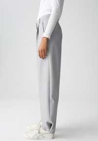 Gray pleated trousers with a tailored fit, featuring a flat front and side pockets, paired with white sneakers. Smooth fabric texture.
