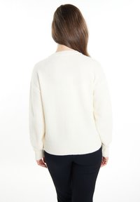 Světlý krémový svetr s žebrovaným spodním lemem a manžetami, který má volný střih a jemnou texturu. Zadní pohled ukazuje jednoduchý, minimalistický design.