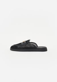 Sorte mesh slip-on sko med flad sål, dekoreret med en glat læderrem og guldhardware. Minimalistisk design med en tekstureret overflade.