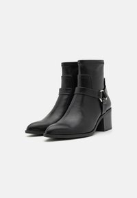 Black leather ankle boots with a pointed toe, narrow shaft, and a chunky heel. Features a decorative strap and buckle detail.