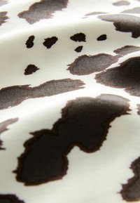 Tissu à motif léopard présentant une texture lisse avec de grandes taches brunes sur un fond crème, mettant en valeur des formes et contours irréguliers.