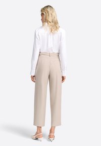 Camicia bianca a maniche lunghe abbinata a pantaloni beige a vita alta. I pantaloni presentano un taglio dritto, una texture sottile e dettagli con tasche posteriori.