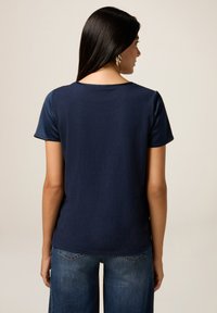 T-shirt blu navy con maniche corte, caratterizzato da una texture liscia e un collo rotondo. Abbinate a jeans blu, viste da dietro.