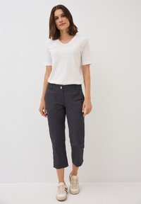 T-shirt bianca a V con maniche corte, abbinata a pantaloni neri tagliati a metà gamba con chiusura a bottone e tasche, completata da sneaker beige.