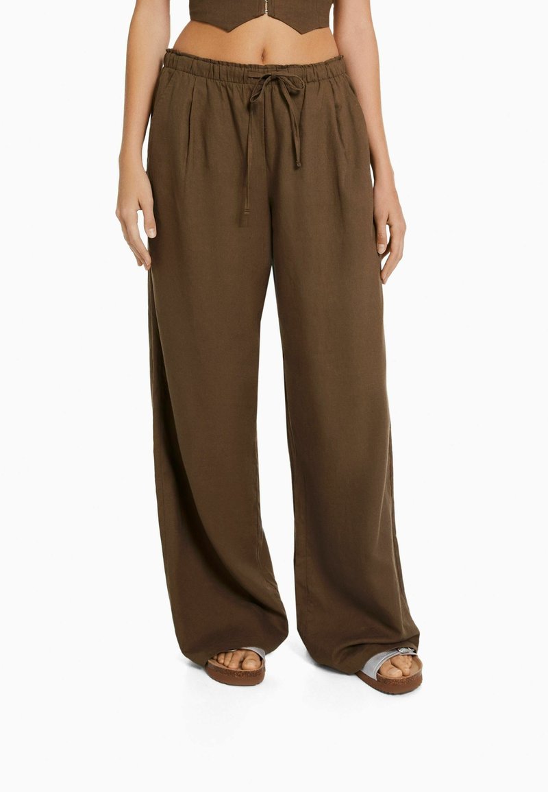 Pantalons marron à jambe large avec une taille à cordon de serrage et des plis devant, fabriqués en tissu léger. Accentué par une texture lisse et une coupe décontractée.