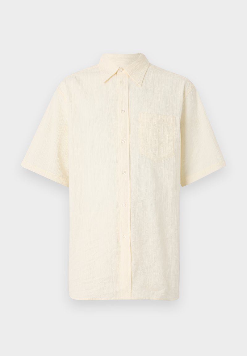 Camisa de manga corta con botones en un color crema pálido, fabricada con un tejido texturizado, que presenta un bolsillo en el pecho y un cuello clásico.