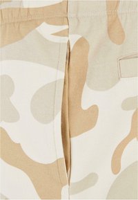 Beige camo-patterned fabric with smooth texture and contrast stitching. Features a side seam and a small patch pocket.