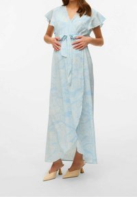 Abito avvolgente azzurro chiaro con maniche corte a volant, motivo floreale in crema, fissato con un nastro in vita. Abbinato a tacchi beige chiaro.