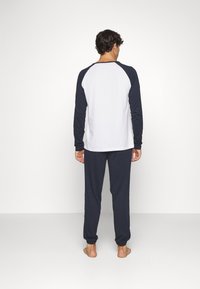 Heren loungewear set met een witte lange mouwen top en navy mouwen, en bijpassende navy broek, gemaakt van zachte stof met een ontspannen pasvorm.