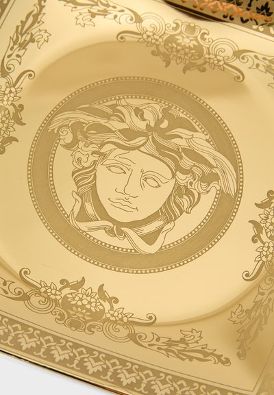 Χρυσό διακοσμητικό πιάτο με πολύπλοκο ανάγλυφο σχέδιο προσώπου περιτριγυρισμένο από φυτικά μ�οτίβα και πλαίσια. Λείος, λαμπερός επιφάνεια.