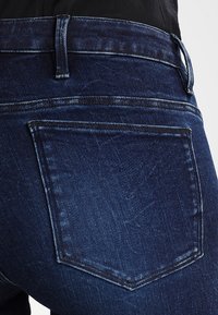 Mörkblå denimjeans med en klassisk femficksdesign, synlig sömnad och en något blekt textur vid fickområdet.
