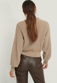 Beżowy, oversize sweter dzianinowy z prążkowanym dołem i balonowymi rękawami, w połączeniu z brązowymi skórzanymi spodniami, widok z tyłu.