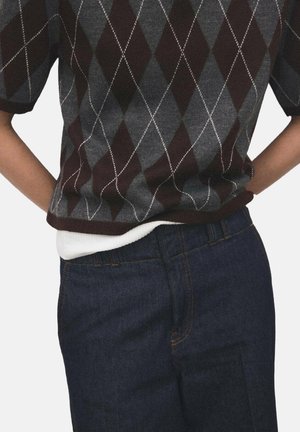 Pull avec un motif en losanges bordeaux foncé et gris, à manches courtes, texture tricotée ; associé à un jean en denim foncé. Une couche blanche est visible au niveau de la taille.