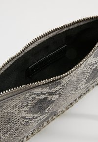 Péněženka se vzorem hada na zip s černou látkovou podšívkou a viditelnou značkovou etiketou uvnitř.