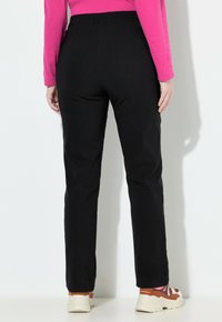 Zwarte broek met een gestructureerde pasvorm, mid-rise tailleband en een rechte pijp, gecombineerd met witte en kleurrijke sneakers.