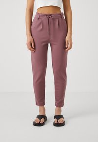 Töjbara, smalnande mjukisbyxor i mauve med dragsko i midjan, sidfickor och en slät yta. Bärs med svarta flip-flop-sandaler.