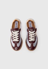 Par tenisica s bijelim vezicama, burgundskom lakiranom kožom i bijelom teksturiranom tkaninom, označenim imenom Steve Madden na ulošku i jeziku.