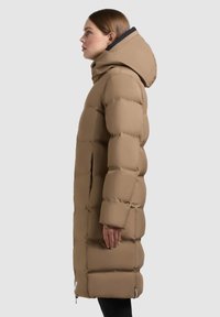 Khaki puchowa kurtka z kapturem, z pikowaną fakturą, bocznymi kieszeniami oraz lekko wydłużonym krojem. Gładka struktura.