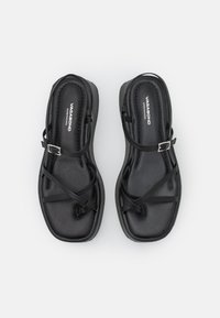 Sorte sandaler med flat såle, med flere kryssede stropper og en justerbar spenne. Glatt tekstur og moderne design.