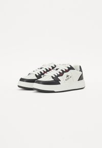 Weiße und schwarze Sneakers mit durchbrochener Detailierung, strukturiertem Leder, flachen Schnürsenkeln und einer robusten Sohle. "REPLAY"-Logo an der Seite.