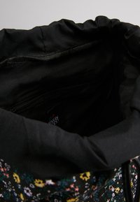 Sac en tissu noir avec un motif floral aux accents roses, jaunes et verts. Fermeture à cordon et poche intérieure zippée. Texture lisse.