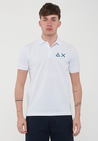 Polo bianco realizzato in cotone, caratterizzato da un colletto a tre bottoni e maniche corte. Ricamo del logo geometrico blu sul lato sinistro del petto.