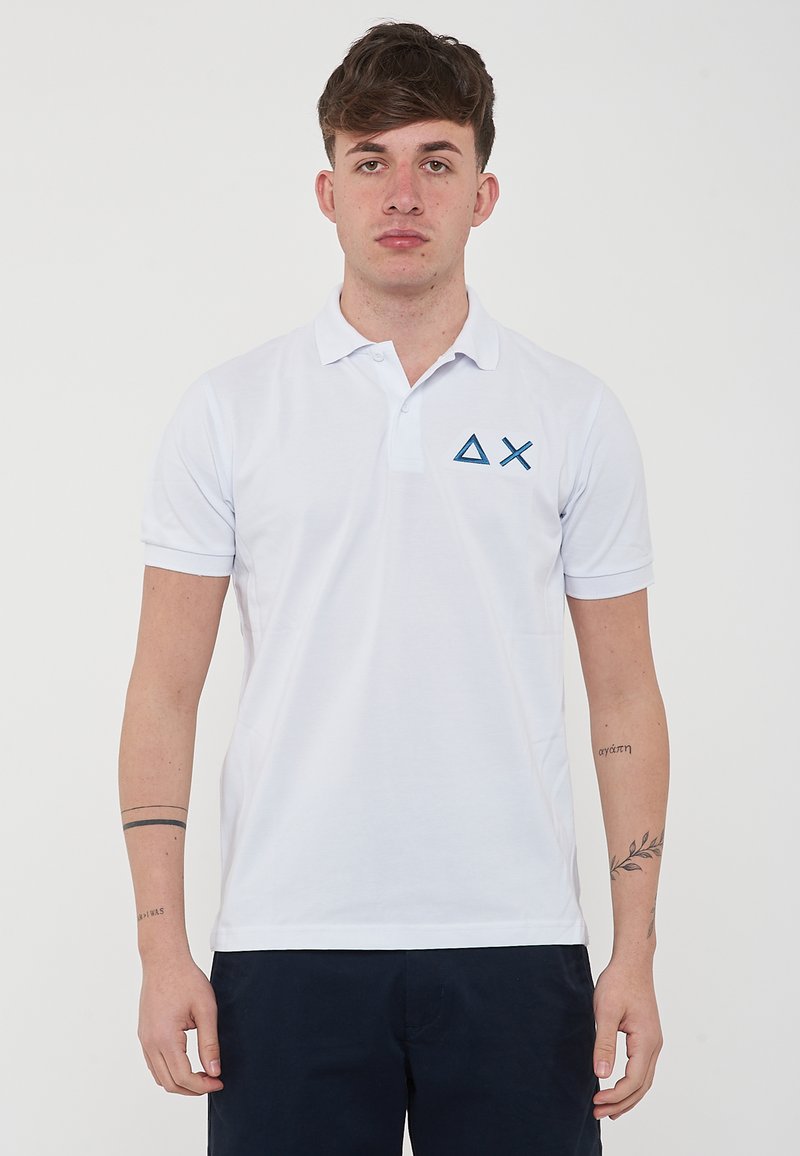 Polo bianco realizzato in cotone, caratterizzato da un colletto a tre bottoni e maniche corte. Ricamo del logo geometrico blu sul lato sinistro del petto.
