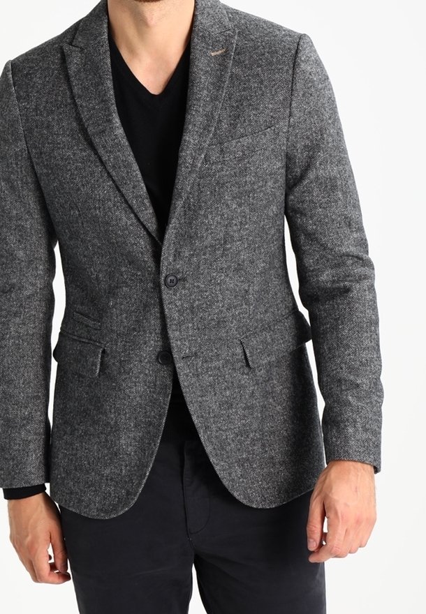 Grau melierte Blazer aus Tweed mit strukturiertem Finish, Ein-Knopf-Verschluss, zwei Taschen vorne und schmalem Reversdesign. Kombiniert mit einem schwarzen Hemd.
