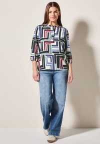 Blusa multicolor con patrones geométricos, con cuello redondo y mangas de tres cuartos, combinada con jeans de pierna ancha en azul claro.