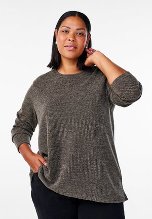 Brown textured knit sweater with a round neckline and long sleeves, featuring a slightly curved hemline. Black pants complete the outfit.