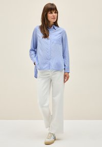 Blue and white striped button-up shirt with long sleeves, a chest pocket, paired with white wide-leg pants and beige sneakers.