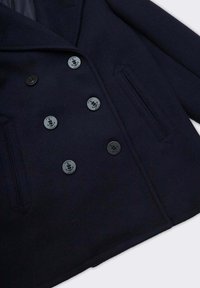 Cappotto doppiopetto in misto lana blu navy con bottoni neri, rever con intaglio, tasche con pattina e fodera interna liscia.