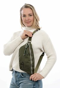 Borsa a rete verde con chiusura a zip, tracolla regolabile e accento logo nero, esposta su uno sfondo bianco uniforme.