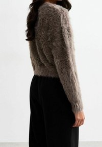 Suéter marrón peludo con mangas largas, con una textura suave y un diseño corto, combinado con pantalones negros de cintura alta.