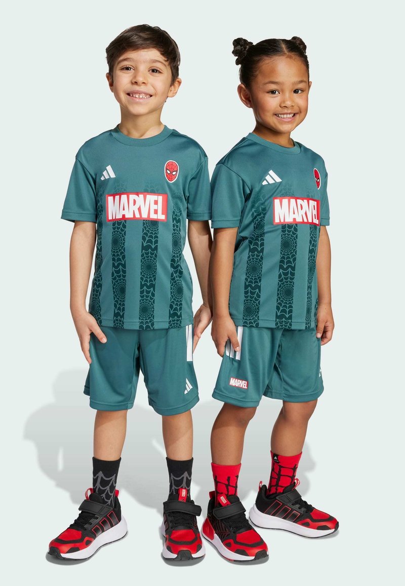Due bambini indossano magliette da calcio turchesi con i loghi di Spider-Man e Marvel, caratterizzate da un design testurizzato. Hanno scarpe rosse e nere con calze a motivi.