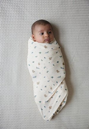 Bebé envuelto cómodamente en un arrullo de color crema con pequeños patrones de animales y hojas, acostado sobre una manta gris texturizada.