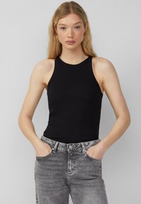 Schwarzes geripptes Tanktop mit hochgeschlossenem Kragen und ärmellosem Design, kombiniert mit grauen hochgeschnittenen Jeans. Schlichte und enganliegende Form.