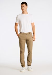 Chinos beige de corte slim, con dos bolsillos frontales, cierre de botón y una textura suave, combinados con una camiseta blanca de cuello redondo y zapatillas blancas.