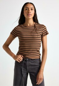 Brun og sort stribet ribbet kortærmet top med rund halsudskæring, parret med mørke grå jeans; stoffet viser et tekstureret mønster.