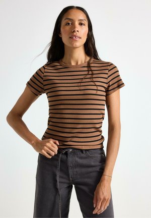 Brun och svart randig ribbad kortärmad topp med rund halsringning, tillsammans med mörkgrå jeans; tyget visar ett strukturerat mönster.