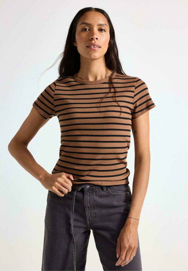 Brun og sort stribet ribbet kortærmet top med rund halsudskæring, parret med mørke grå jeans; stoffet viser et tekstureret mønster.