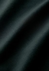 Gros plan d'un tissu lisse et sombre avec des plis doux et une texture subtile créant un motif ombragé et fluide.