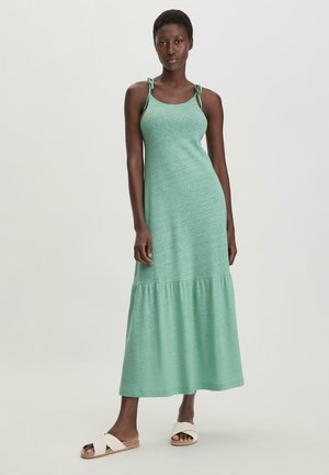 Mint green maxi dress with a relaxed fit, adjustable straps, and a tiered hem. Worn with white cross-strap sandals, smooth texture.