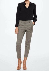 Chemise noire à manches longues avec col, associée à un pantalon slim à carreaux. Des escarpins à lanières beiges complètent la tenue.