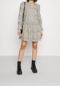 Långärmad, lager-på-lager miniklänning i beige med ett strukturerat mönster, med en nyckelhålsutskärning. Matchad med svarta snörda ankelstövlar.