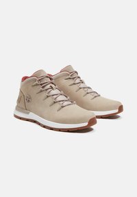 Beige Wanderschuhe mit einer glatten Wildleder-Oberfläche, Gummisohlen und kontrastierenden roten Akzenten an der Knöchelpartie und dem Schnürsystem.