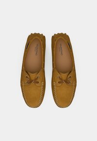 Mocasines de ante marrón con diseño de cordones, costuras en contraste y un forro interior suave. Incluyen el logo en la plantilla.